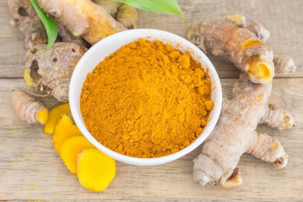 Turmeric powder in a bowl and turmeric root