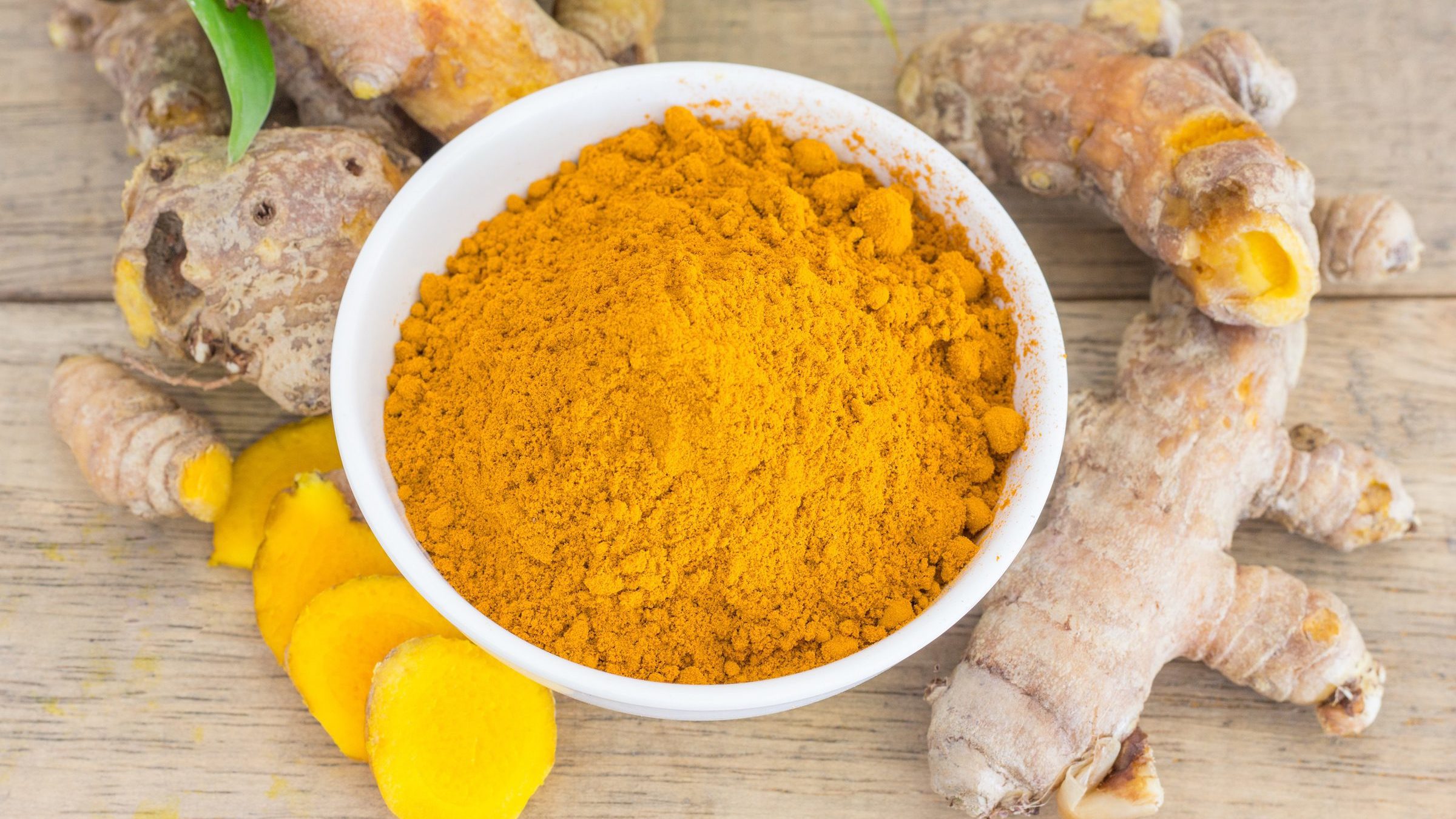 Turmeric powder in a bowl and turmeric root